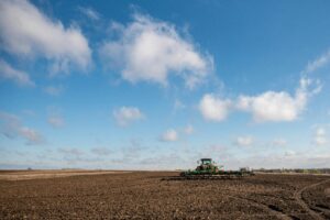 A lone tractor plowing a vast field under a bright blue sky in rural Nebraska.